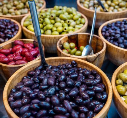Various types of olives displayed in wooden bowls at an outdoor market.