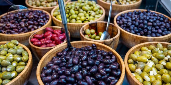 Various types of olives displayed in wooden bowls at an outdoor market.